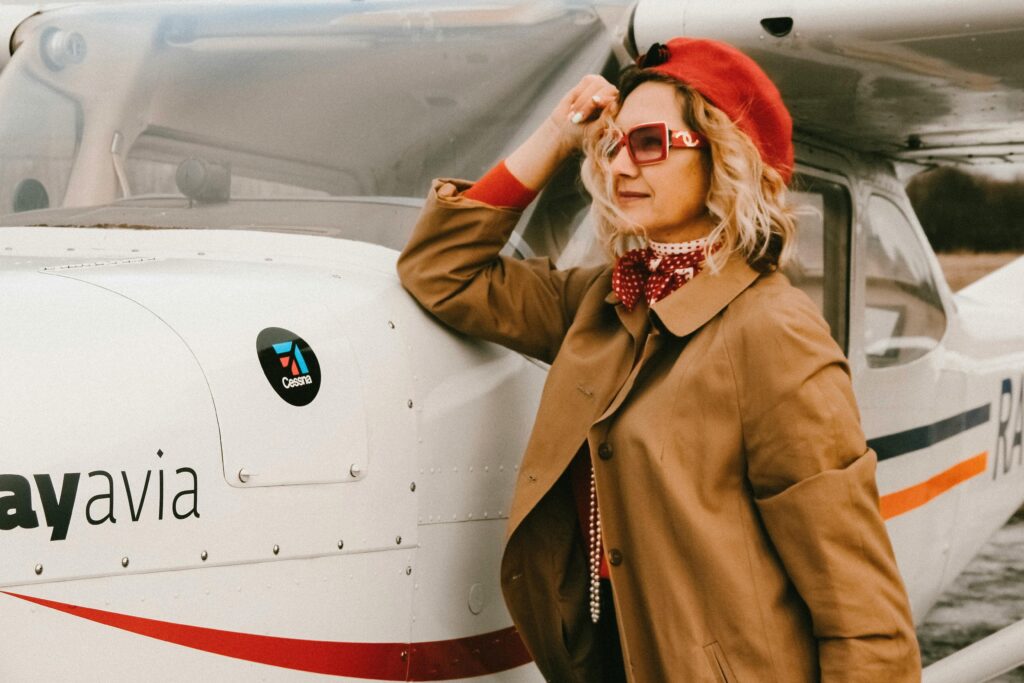 Stylish woman in sunglasses and red beret posing by airplane outdoors.